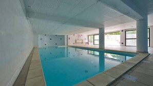An indoor swimming pool with clear blue water, tiled floor, and a ceiling with visible structural beams.