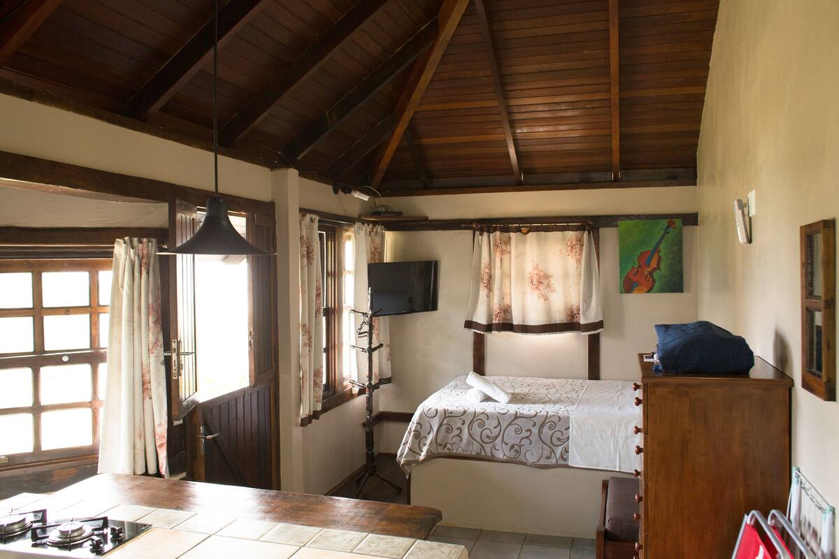 Una habitación con cama, escritorio, silla, televisión y ventana con cortinas.