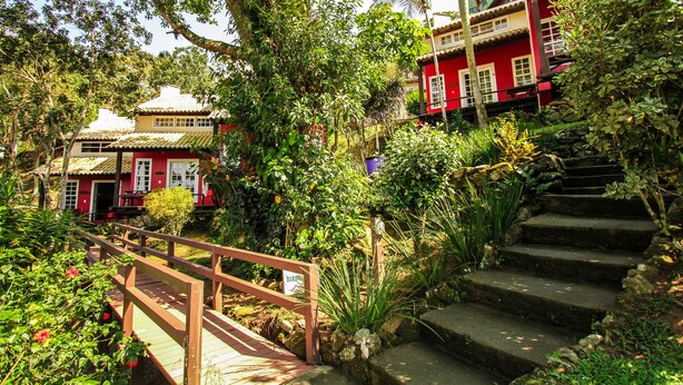 A traditional building with a red facade, a wooden staircase, and lush greenery. - Pousada dos Ingleses (Bombinhas)
