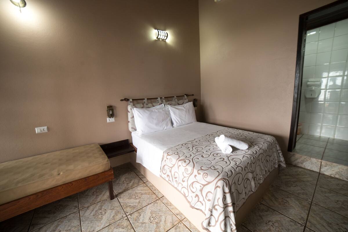 Un dormitorio con cama, un banco, una lámpara de pared y suelo de baldosas.