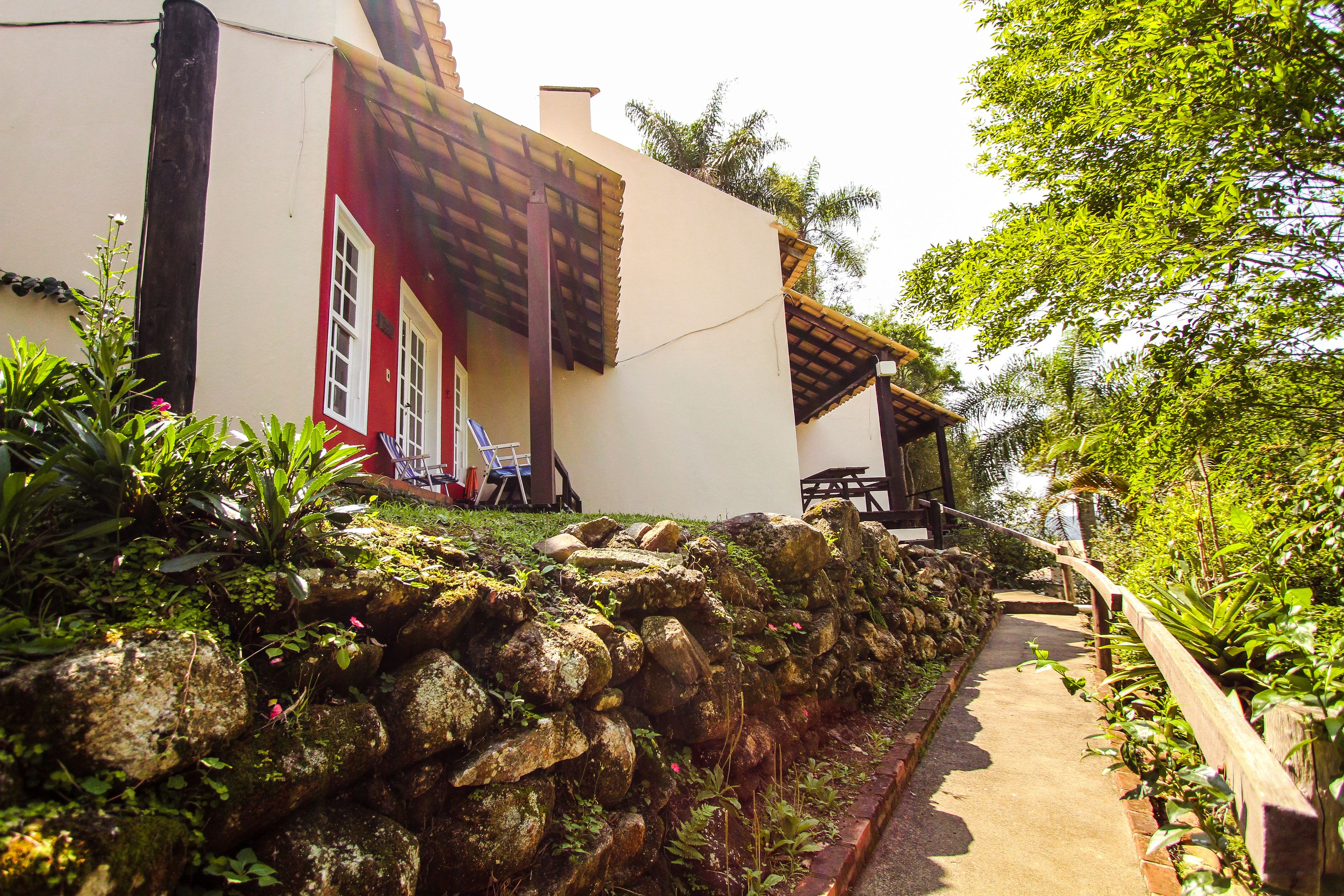 A stone wall, a pathway, and a building with a red door and a wooden pergola.