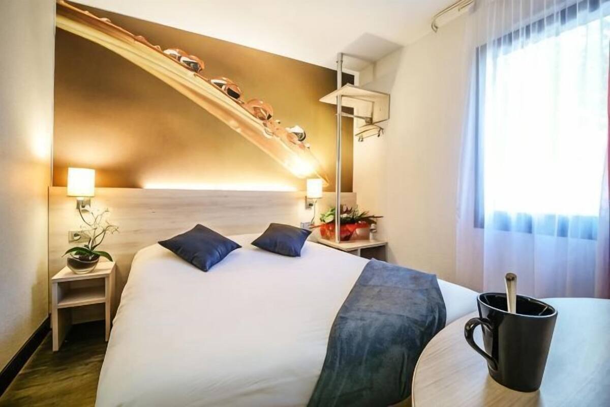A hotel room with a bed, bedside tables, a coffee table, a staircase, and a window with curtains.