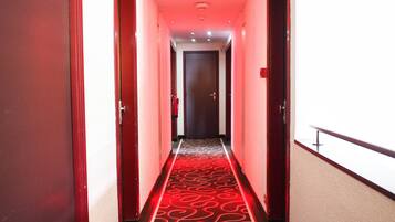 Un pasillo de hotel con alfombra roja, puertas de madera y una puerta oscura al final.
