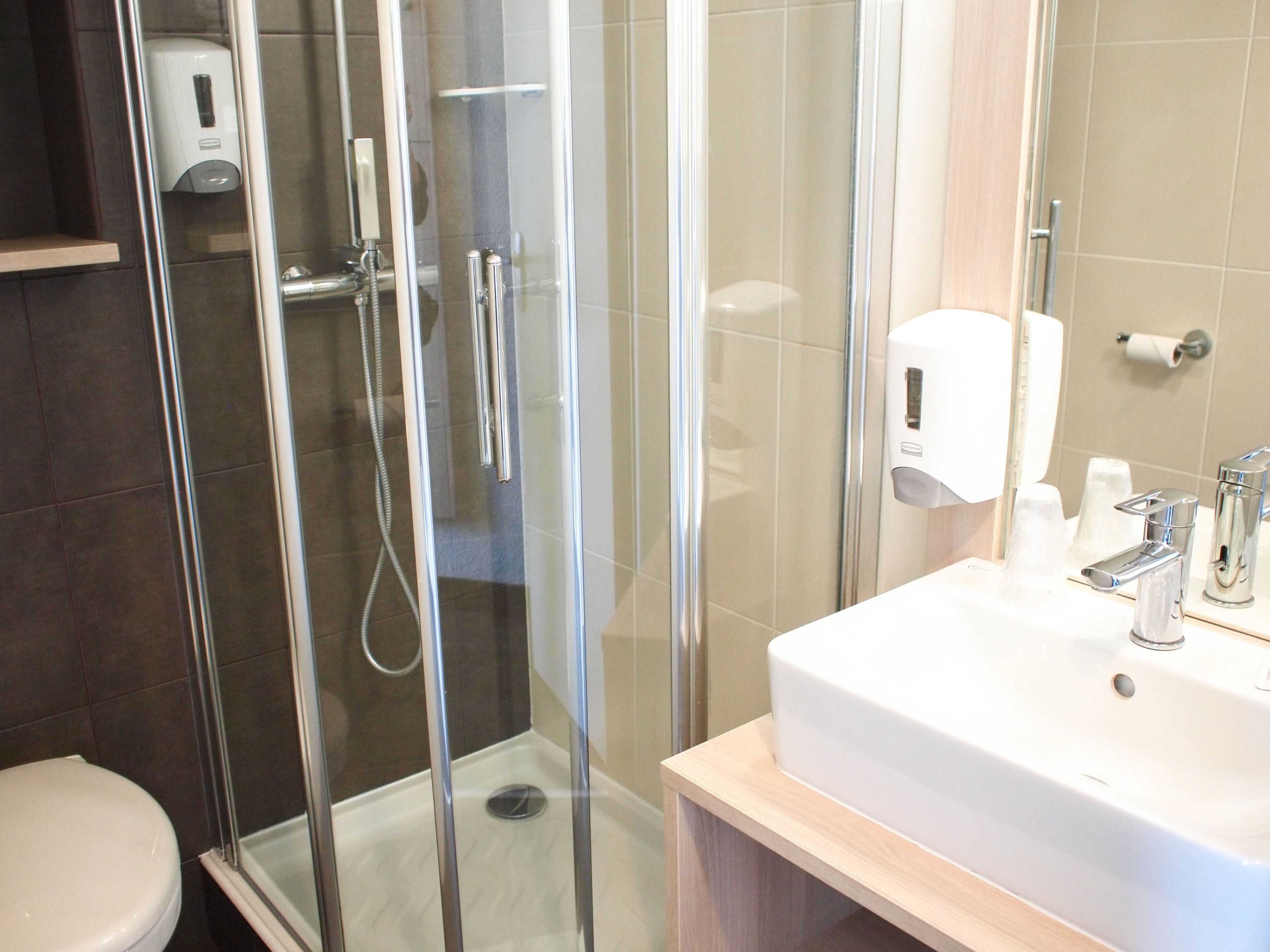 A modern bathroom with a glass-enclosed shower, a white sink with chrome fixtures, and a toilet.