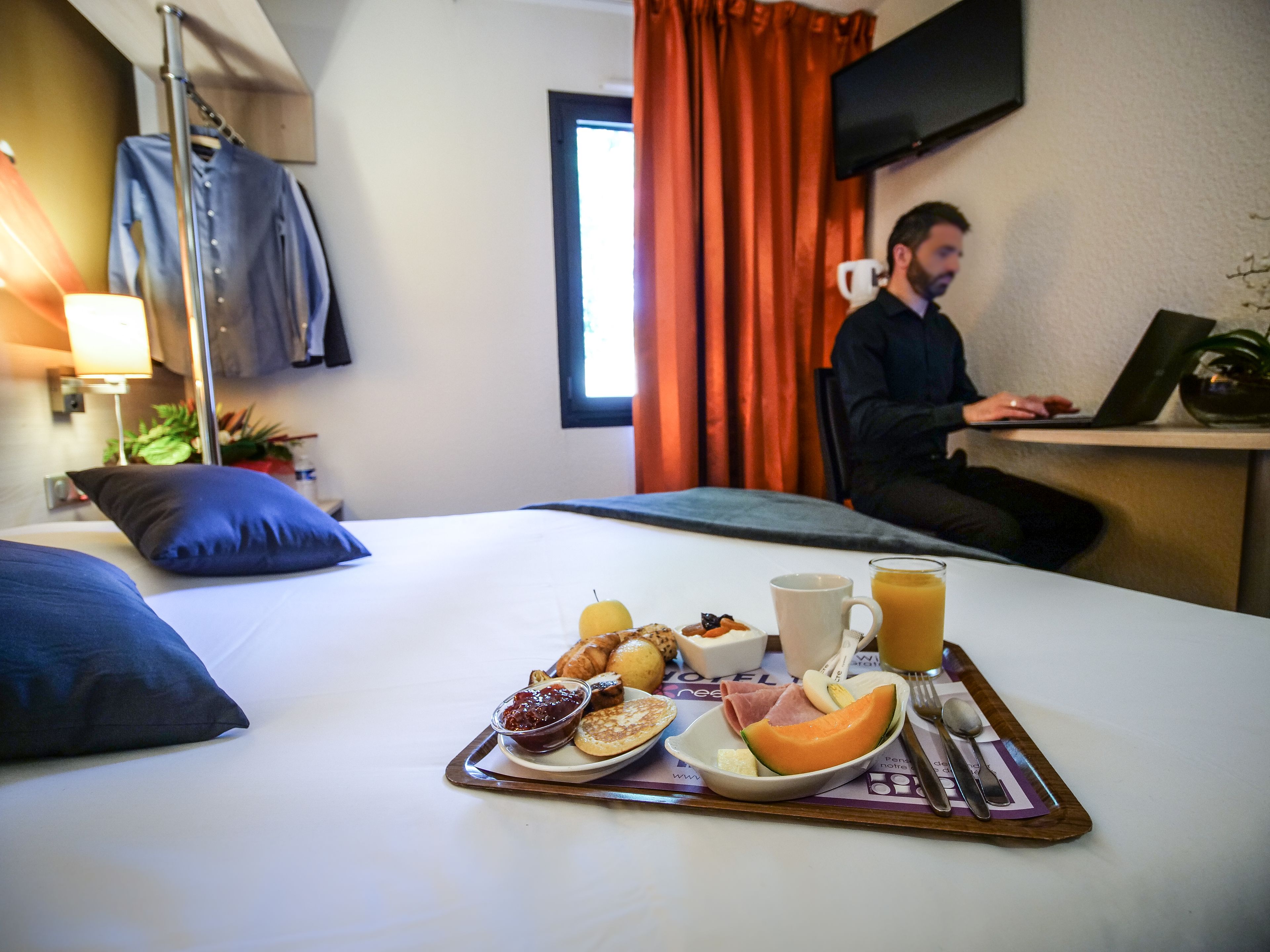 Une chambre d’hôtel avec un lit, un plateau de petit-déjeuner et une personne travaillant sur un ordinateur portable.