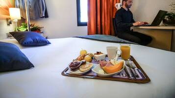 Une chambre d’hôtel avec un lit, un plateau de petit-déjeuner et une personne travaillant sur un ordinateur portable.