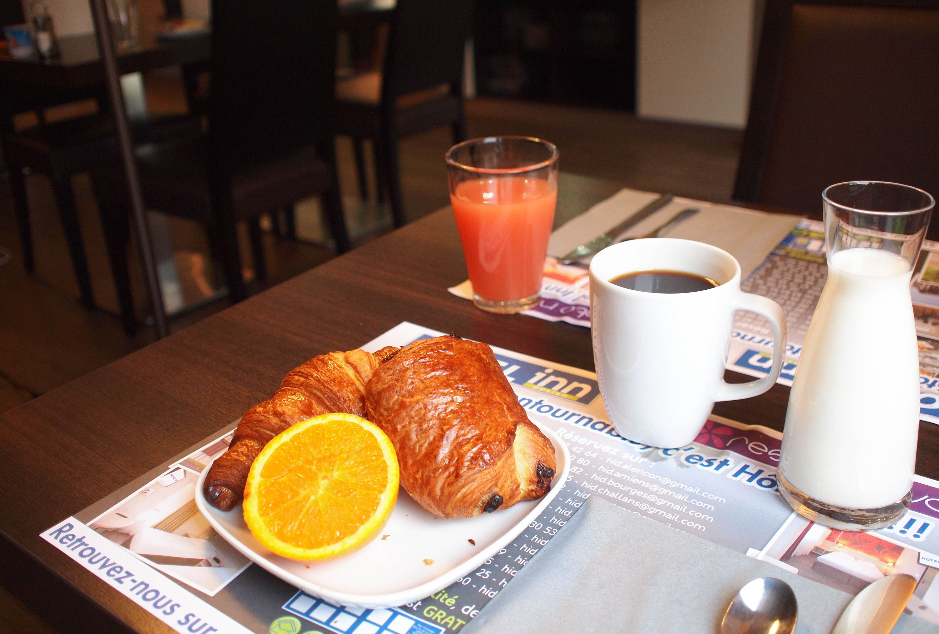 Una escena de desayuno con un croissant, una rodaja de naranja, café y jugo en una mesa.