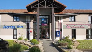 A hotel with a modern design, featuring a prominent entrance with a tiled roof and two visible signs for 'HOTEL INN' and 'nestolo l'escalate'. - Hôtel Inn Design & Restaurant Rochefort (Rochefort)