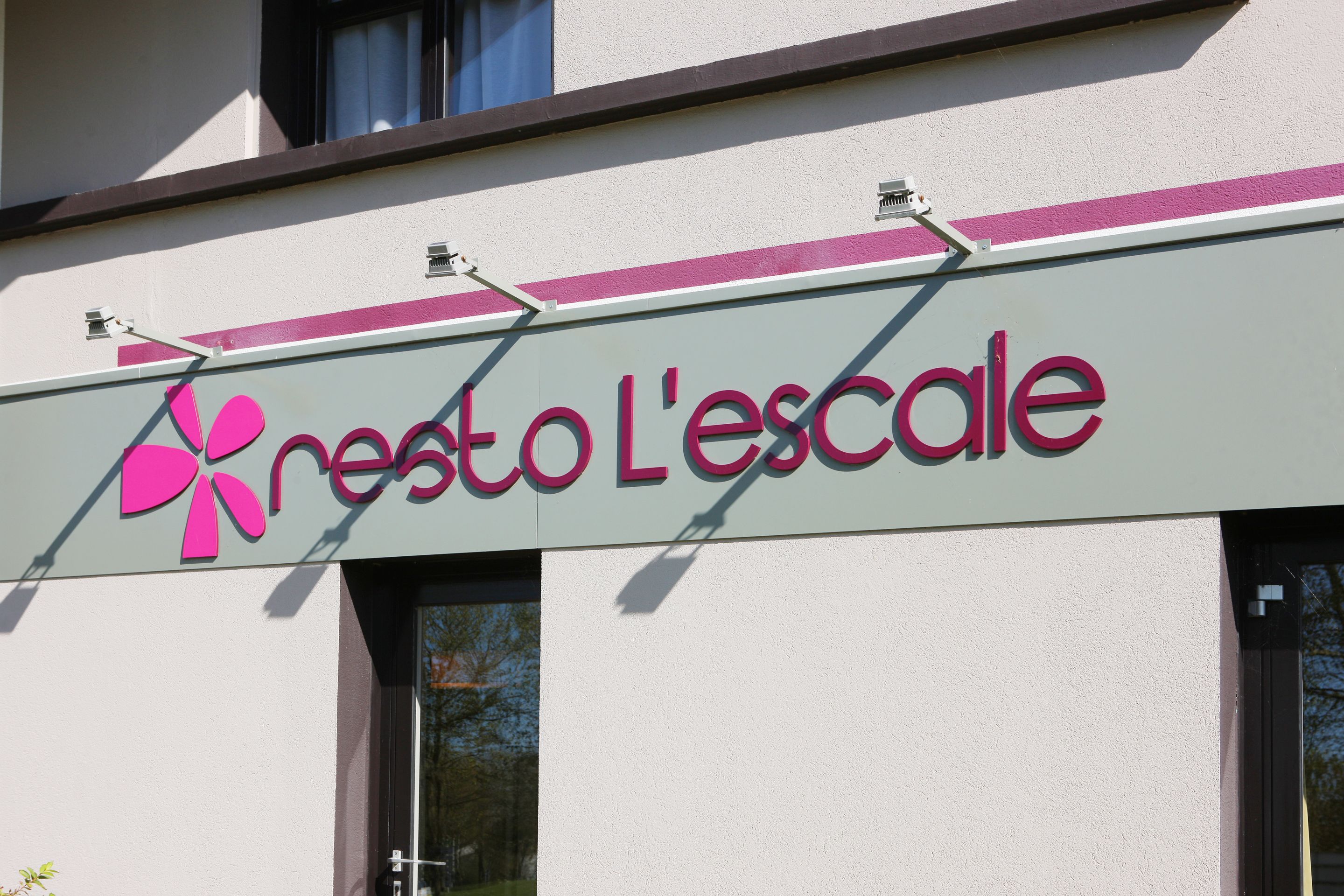 A building with a sign that reads "resto L'escalle" and a pink flower logo.