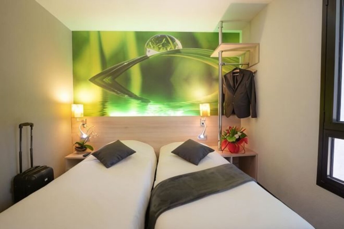 A hotel room with two beds, a wall-mounted coat rack, a small table with a lamp, and a window.