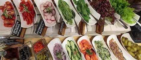 A variety of fresh vegetables and fruits displayed on white plates, with labels in a foreign language.