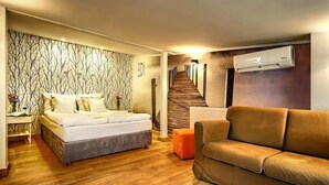 Une chambre à coucher avec un lit, un canapé, un plancher en bois, un mur à motifs et un escalier menant à une autre pièce.