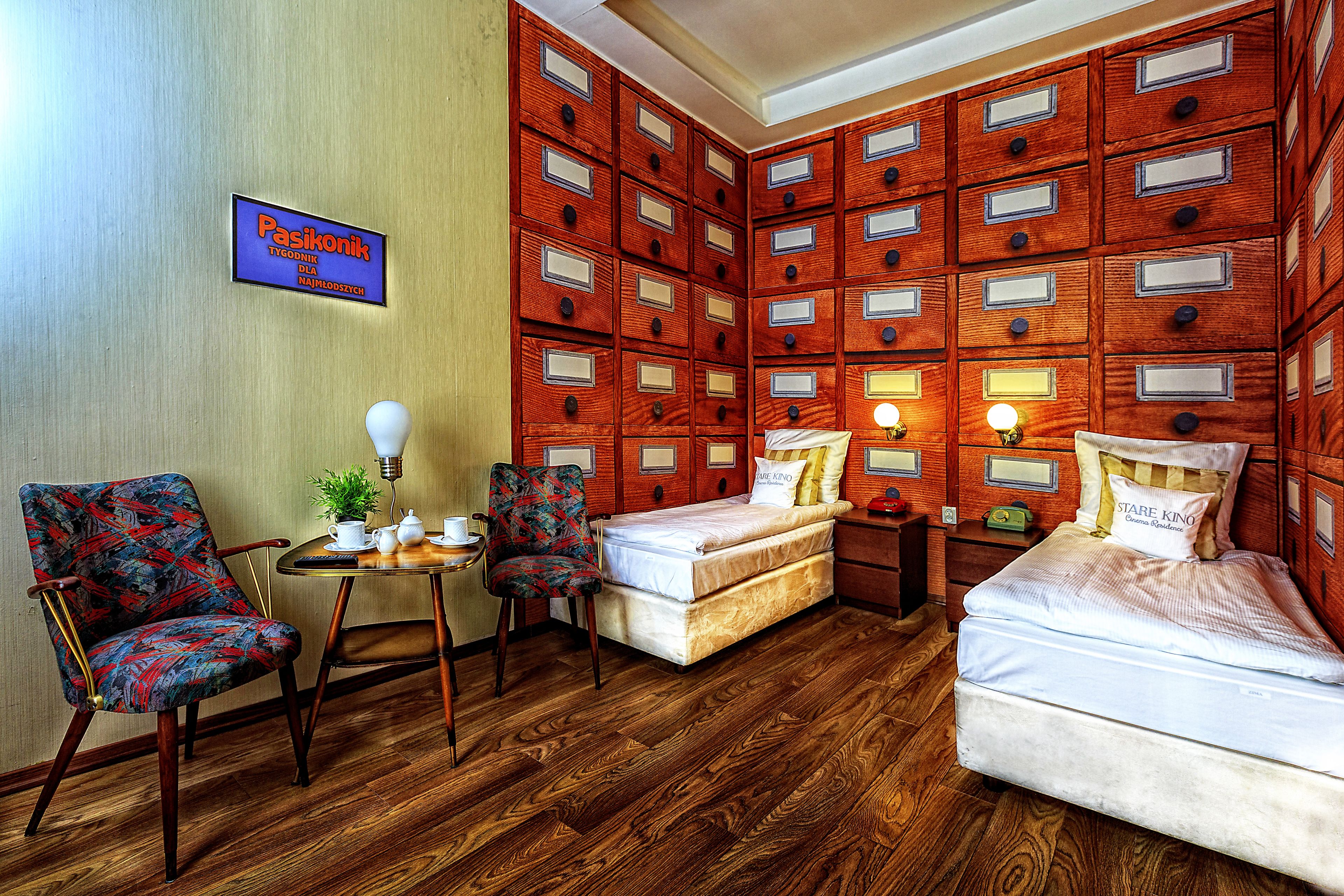A hotel room with a bed, two chairs, a small table with a plant, and a wall of storage drawers.