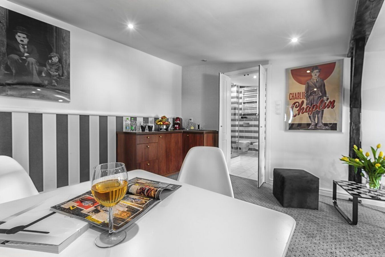 A modern hotel room with a dining area, a kitchen, and a bathroom visible through an open door.