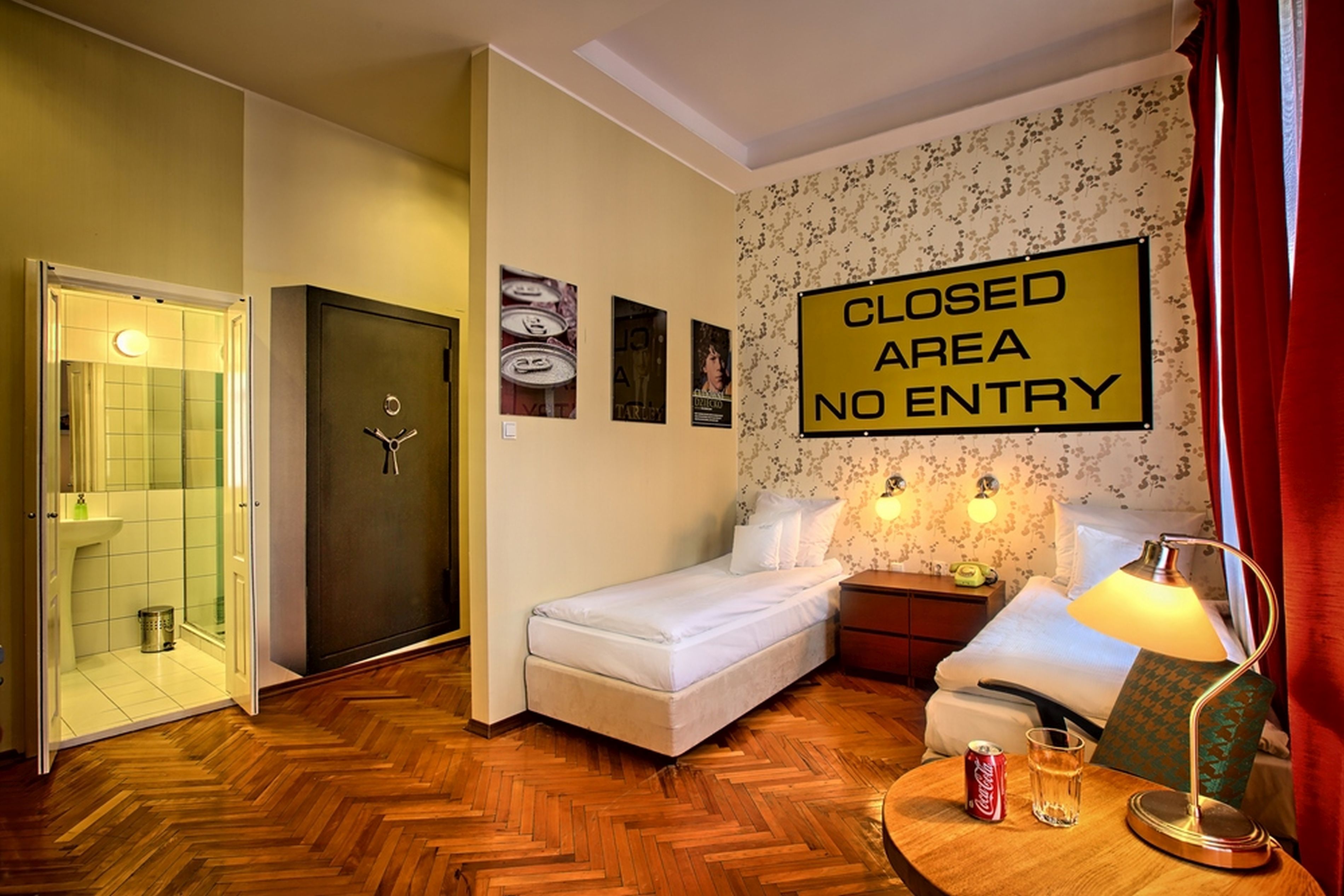 A hotel room with a bed, a nightstand, a lamp, a bottle of Coca-Cola, and a glass. There is a door with a sign indicating a closed area with no entry.