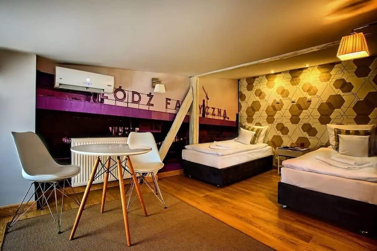 Ein modernes Hotelzimmer mit einem Bett, einem kleinen Tisch mit Stühlen, einem Heizkörper und einer Wand-Klimaanlage.