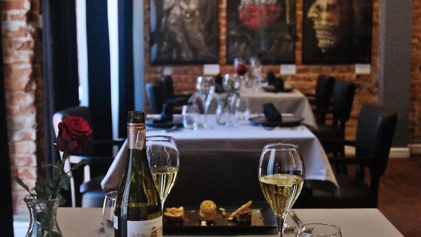 L’intérieur d’un restaurant, avec une table dressée pour le dîner, agrémentée d’une bouteille de vin, de verres et d’une rose.