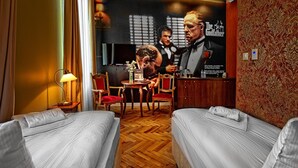 Une chambre d’hôtel avec deux lits, un plancher en bois, une télévision, une petite table avec des chaises et une affiche accrochée au mur.