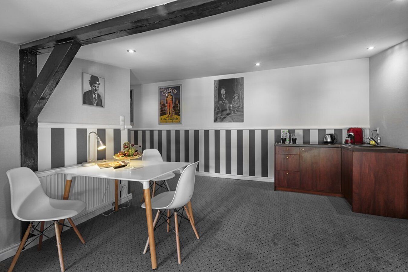 Eine moderne Küche mit Essbereich, mit einem weißen Tisch, grauen Stühlen, einem Holzschrank und einer roten Kaffeemaschine.