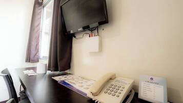 A hotel room with a flat-screen TV mounted on the wall, a telephone, and a sign listing room rates.