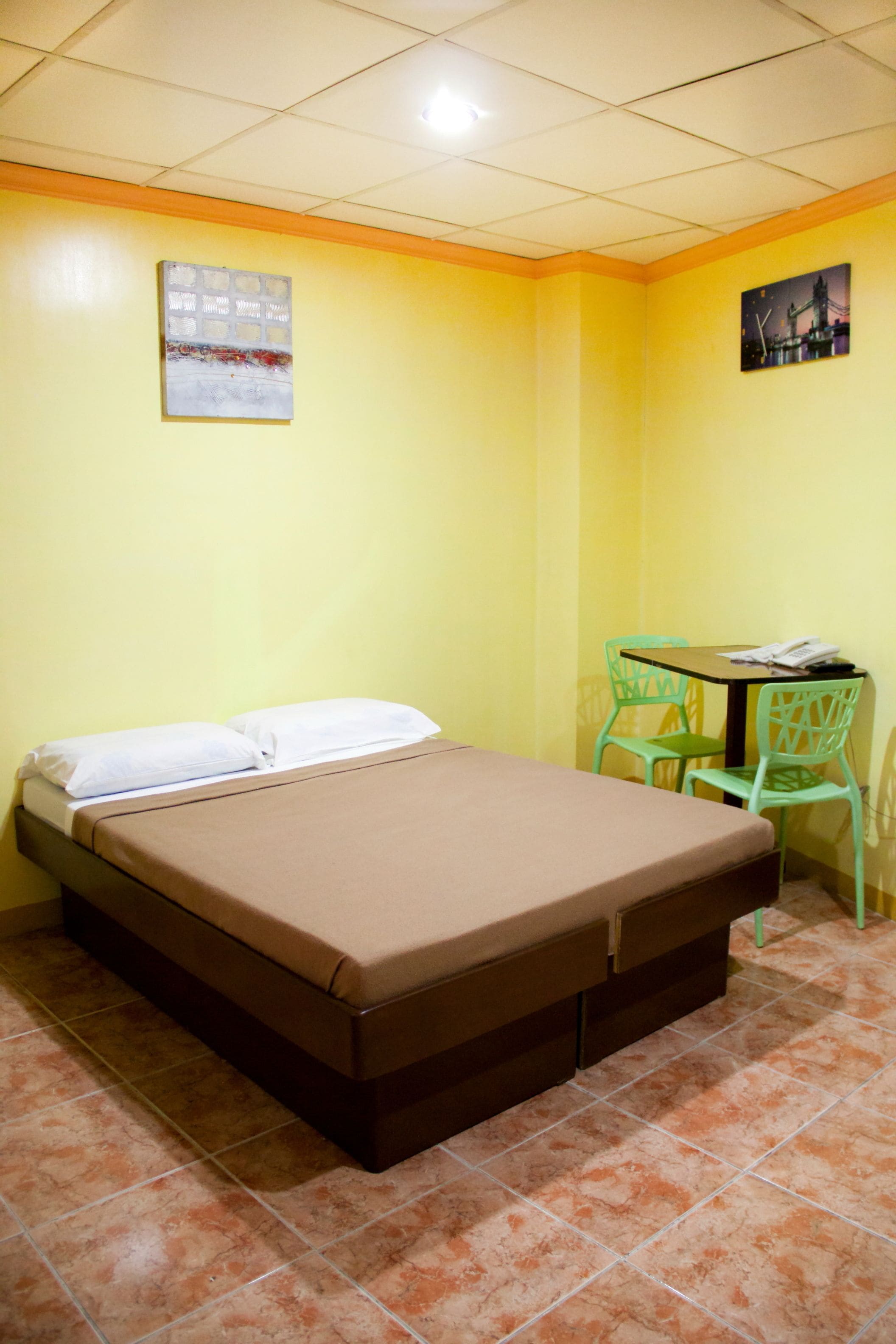 A room with a bed, a small table, two chairs, and artwork on the walls.