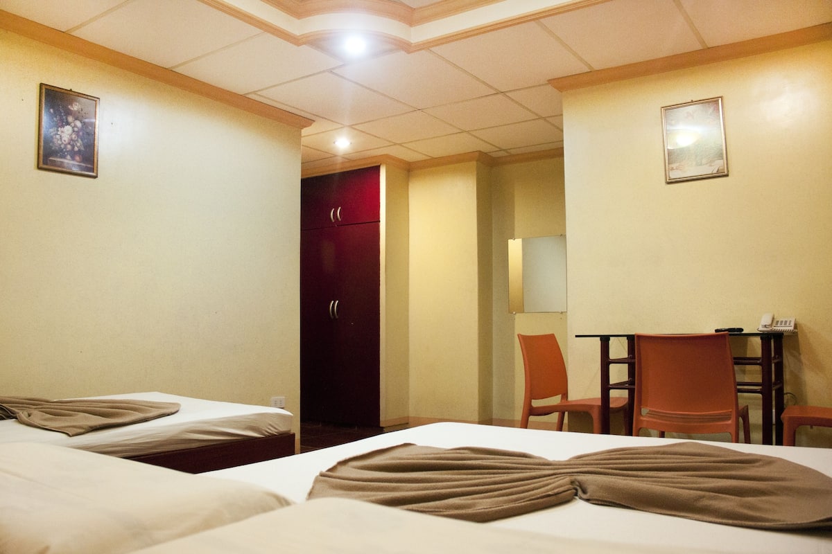 A hotel room with two beds, a desk, a chair, and a door.
