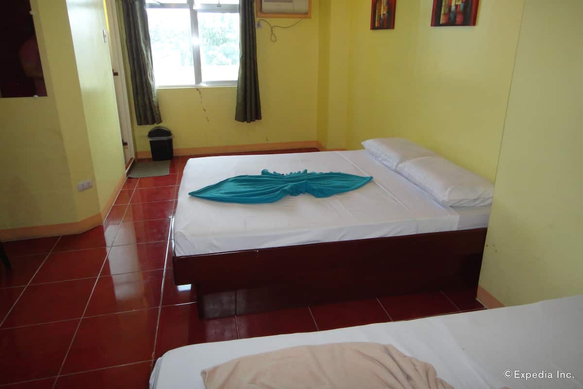 A room with a bed, a window with curtains, a trash bin, and a wall-mounted air conditioner.