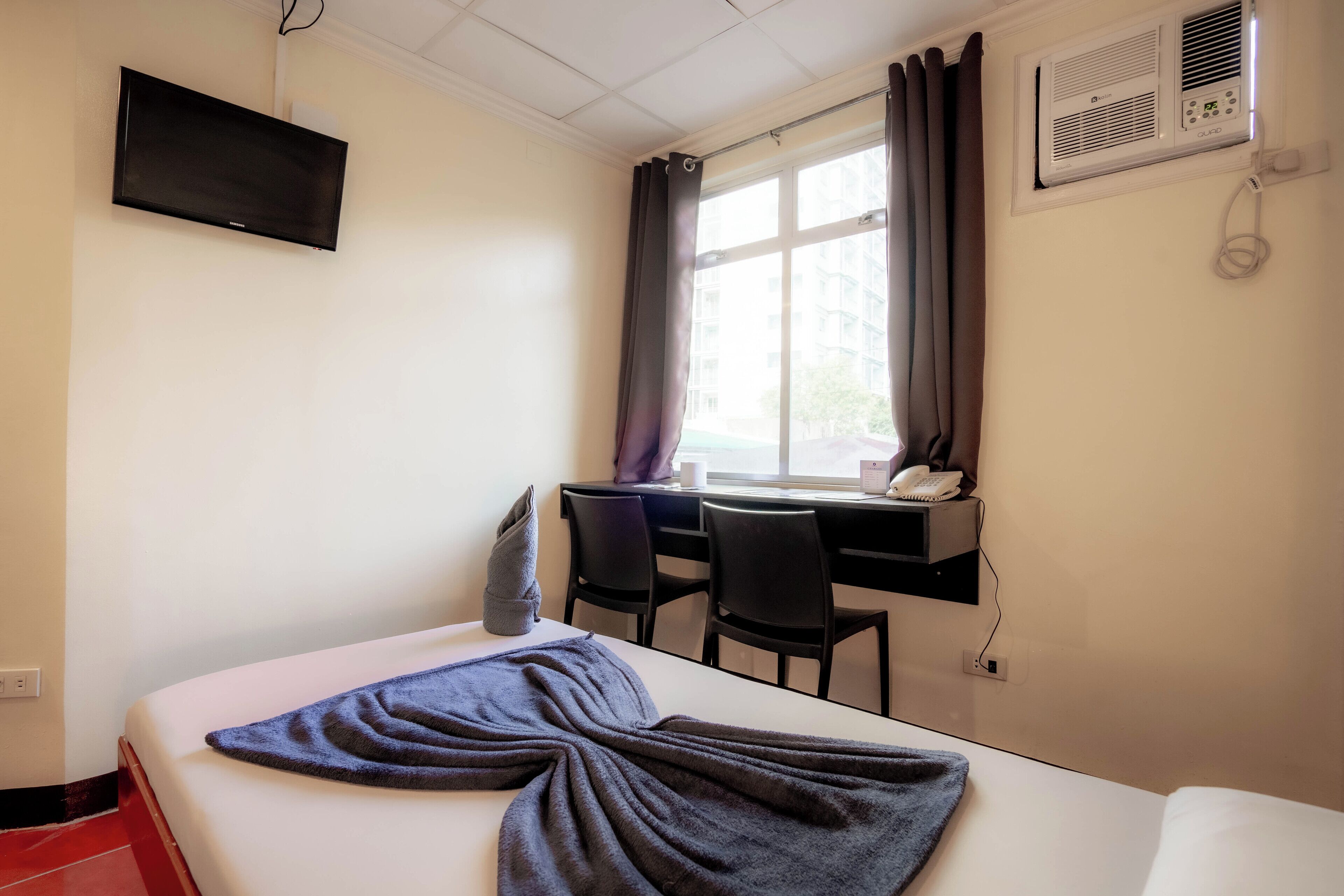 Habitación de hotel con cama, escritorio, silla, televisor y aire acondicionado.