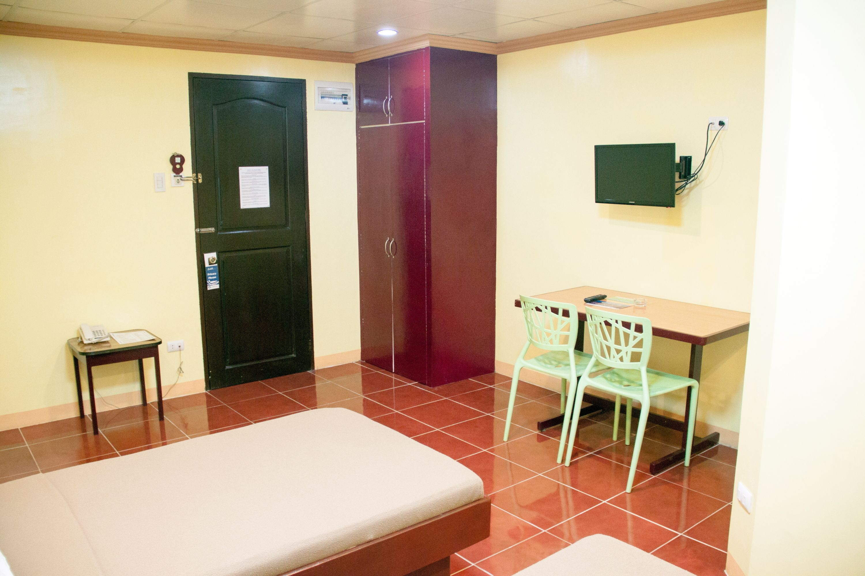A room with a bed, a desk with a chair, a wardrobe, and a television mounted on the wall.