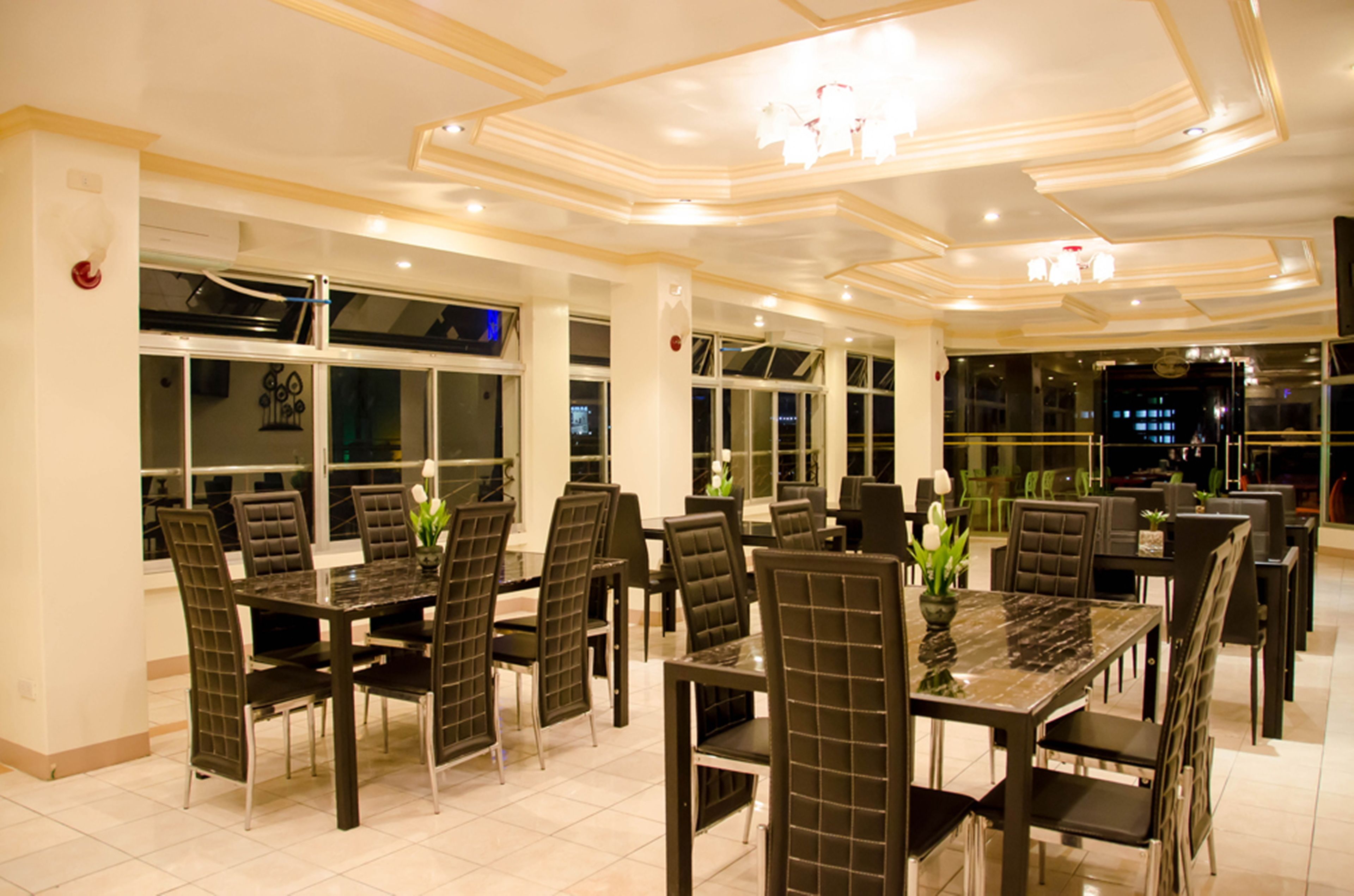 A dining area with multiple tables and chairs, large windows, and a modern ceiling design.