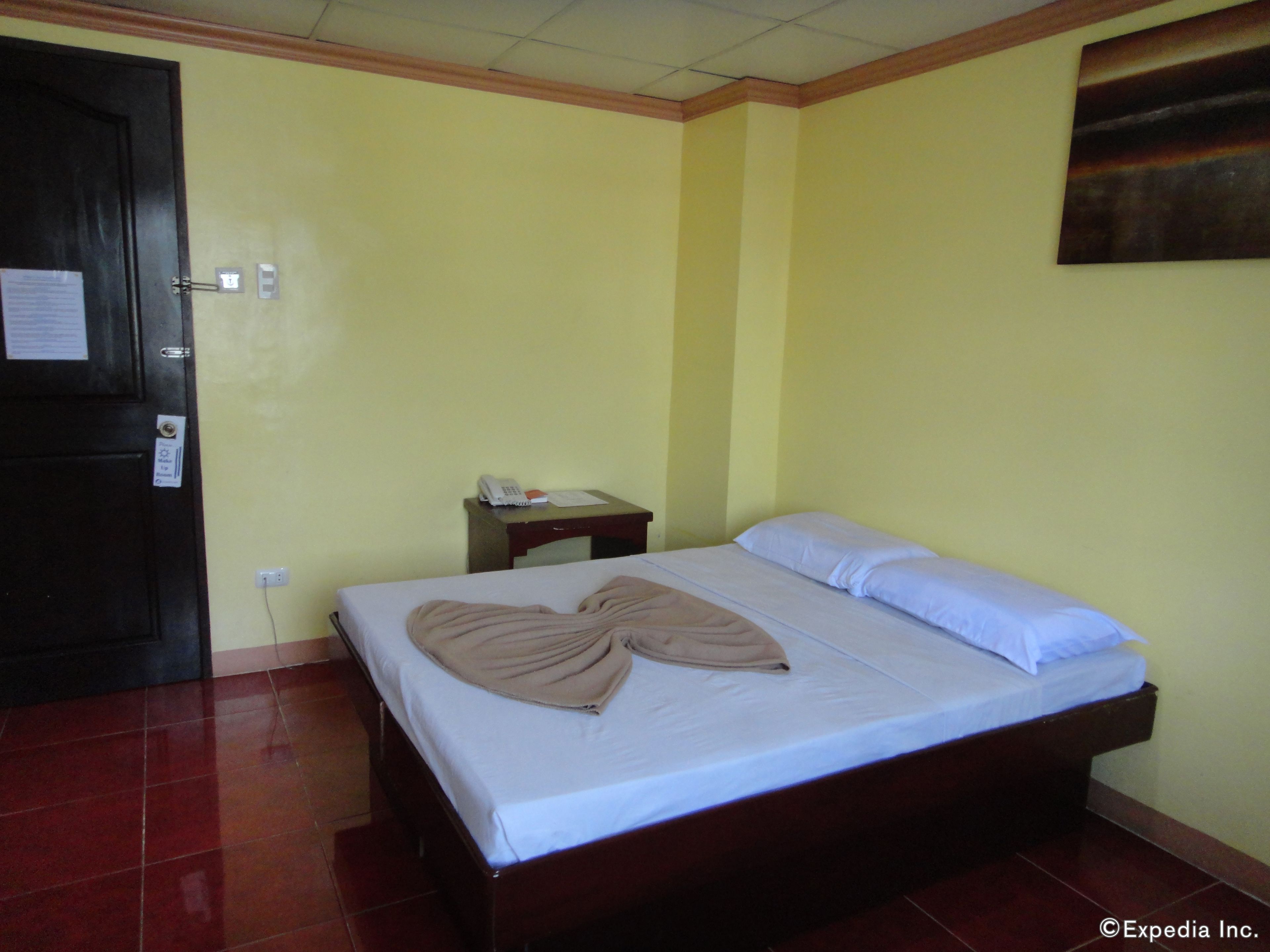 A hotel room with a bed, a bedside table, a phone, and a door with a notice.