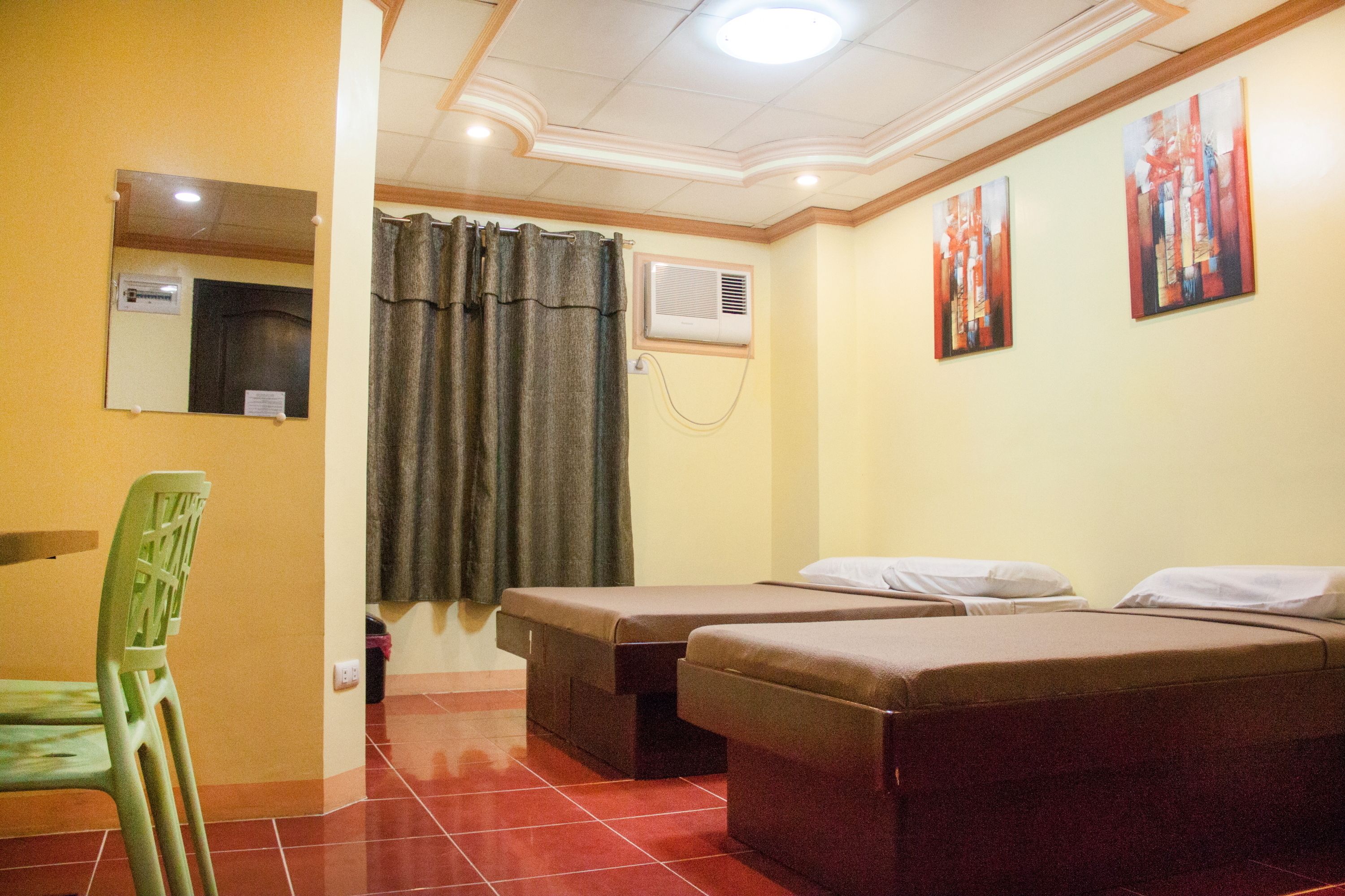Una habitación con dos camas individuales, una silla verde, un espejo y dos cuadros en la pared.