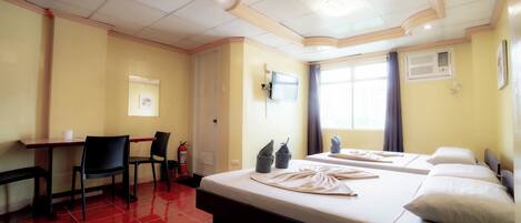 Habitación de hotel con cama, escritorio, sillas, televisor y ventana con cortinas.