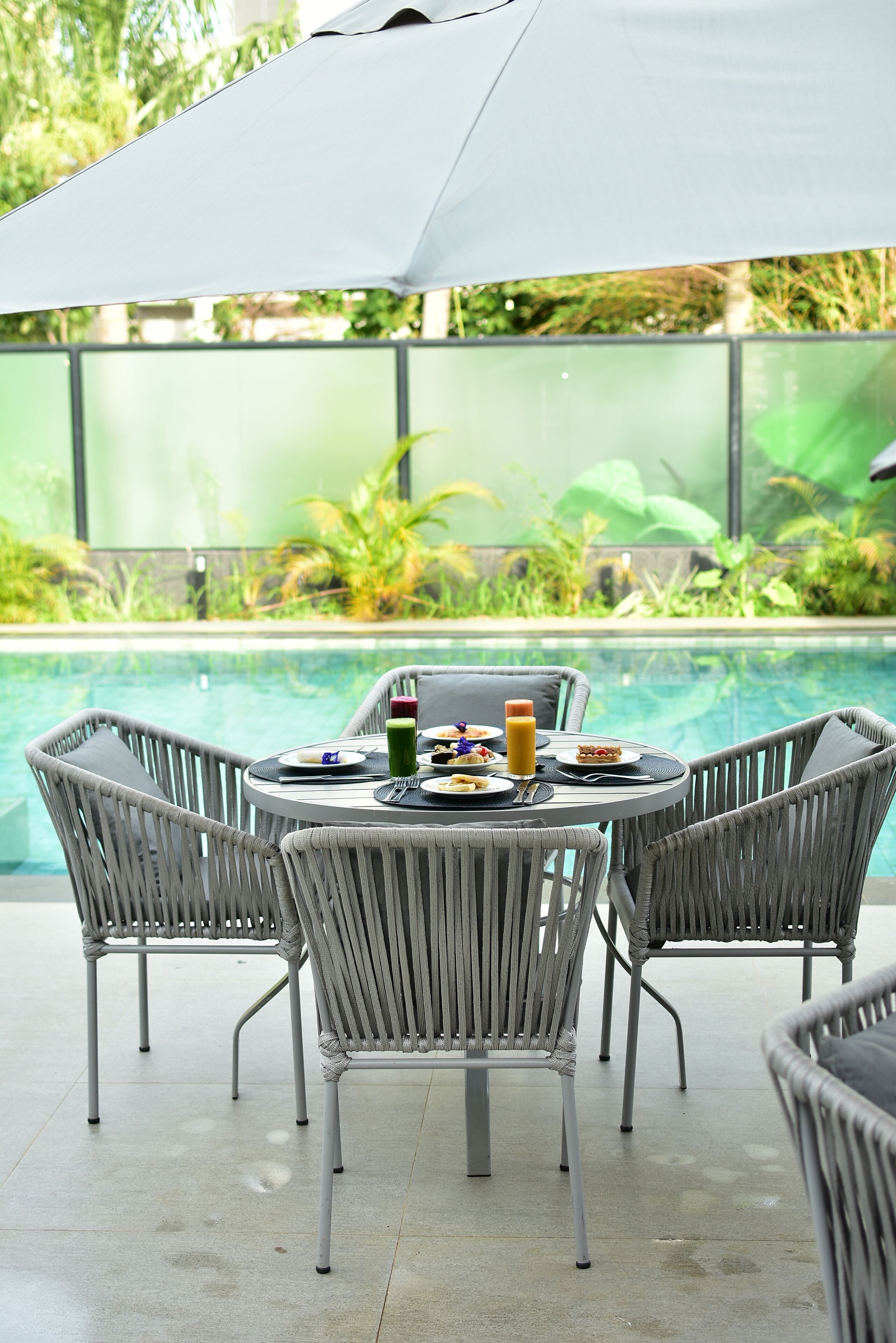 Zona de comedor junto a la piscina con sillas de mimbre y una mesa para dos, con vistas a una alberca.
