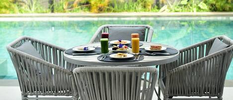 Zona de comedor junto a la piscina con sillas de mimbre y una mesa para dos, con vistas a una alberca.