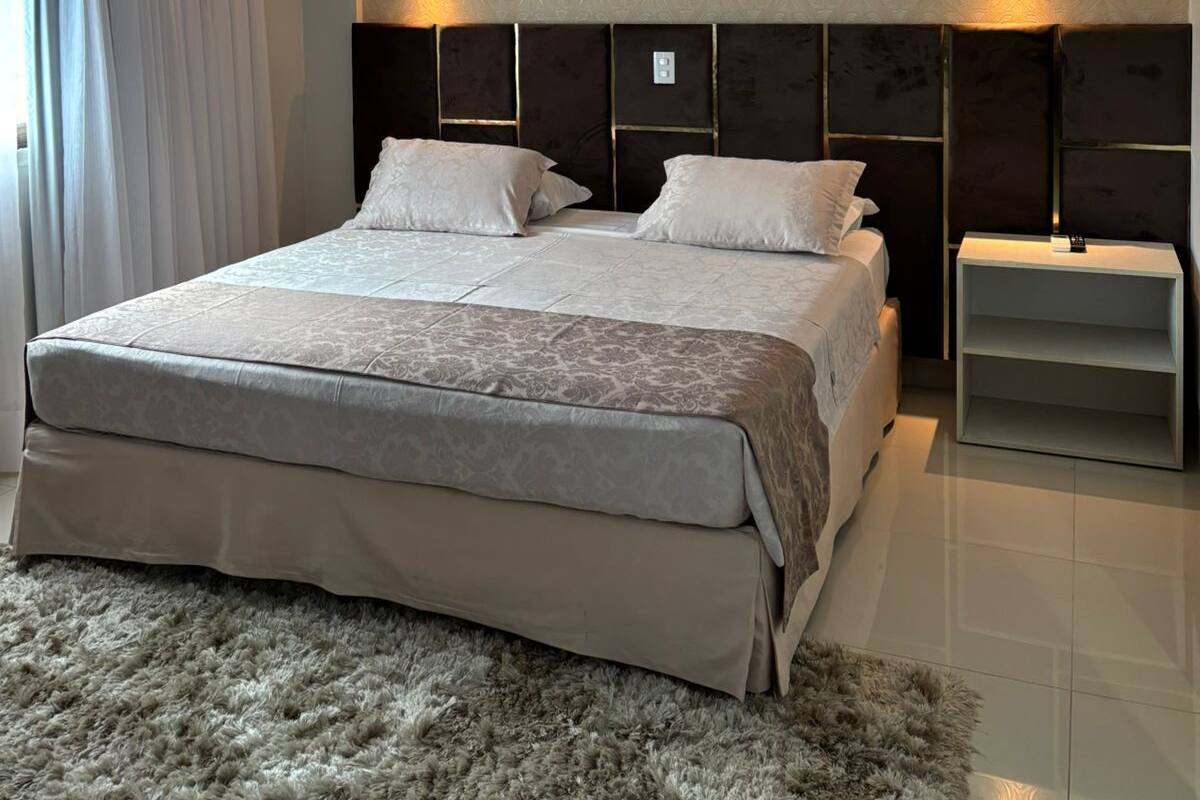 Un dormitorio moderno con una cama grande, dos luces fijadas a la pared, una mesita de noche y una alfombra mullida.