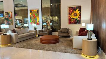 Uma sala de estar moderna com um sofá, poltronas e uma mesa de centro. Há quadros abstratos nas paredes e uma grande janela com vista para o interior.