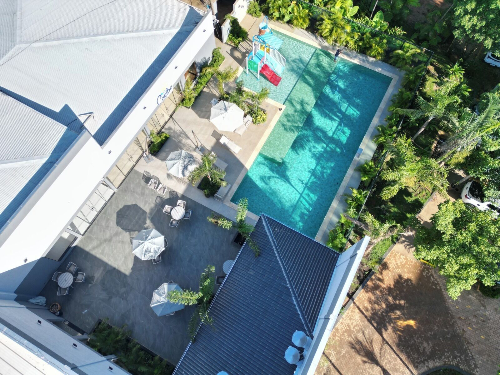 An aerial view of a hotel with a swimming pool surrounded by outdoor seating and greenery.