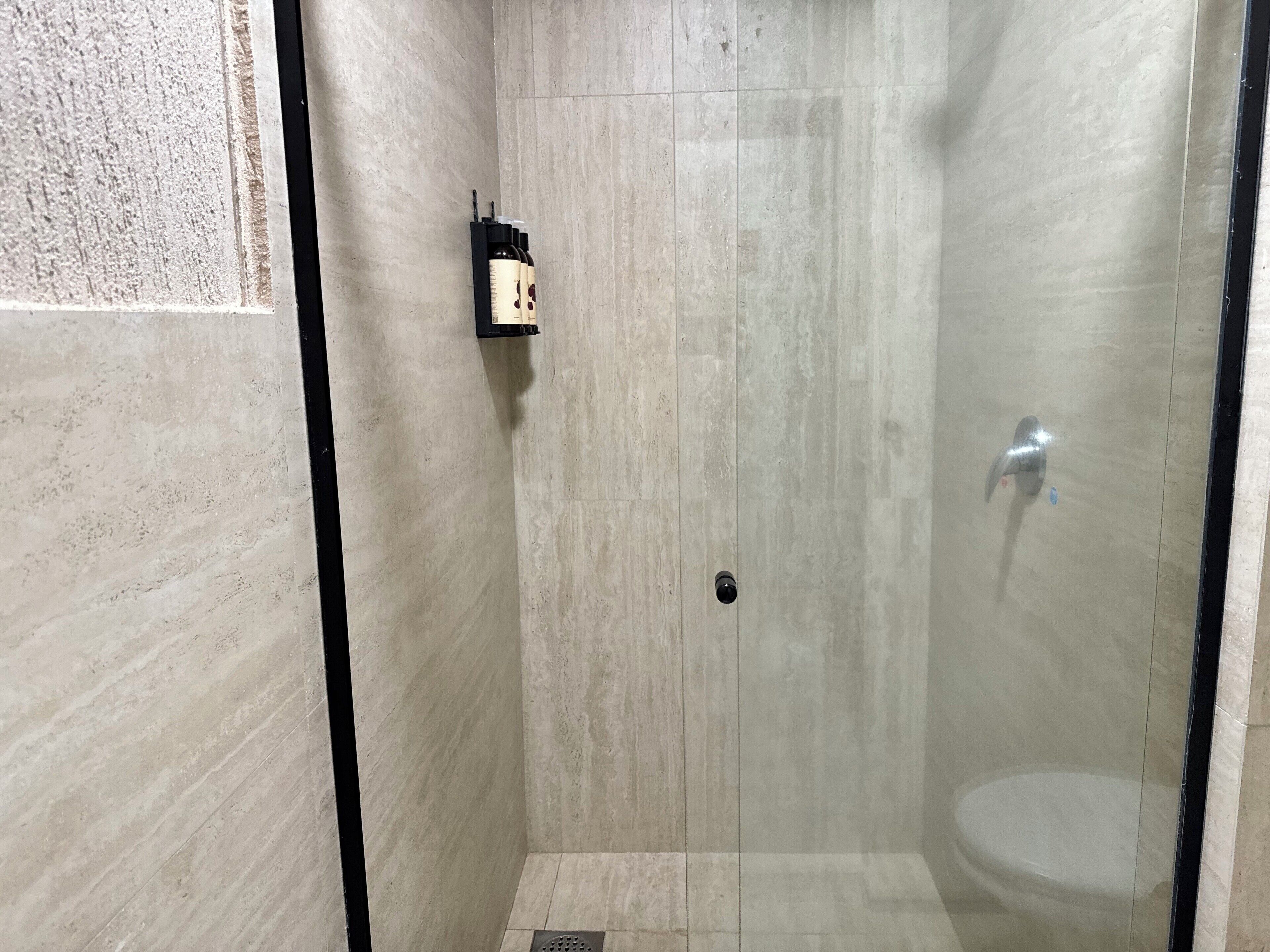 Ducha a pie con mampara de vidrio, paredes con azulejos y un perchero negro.