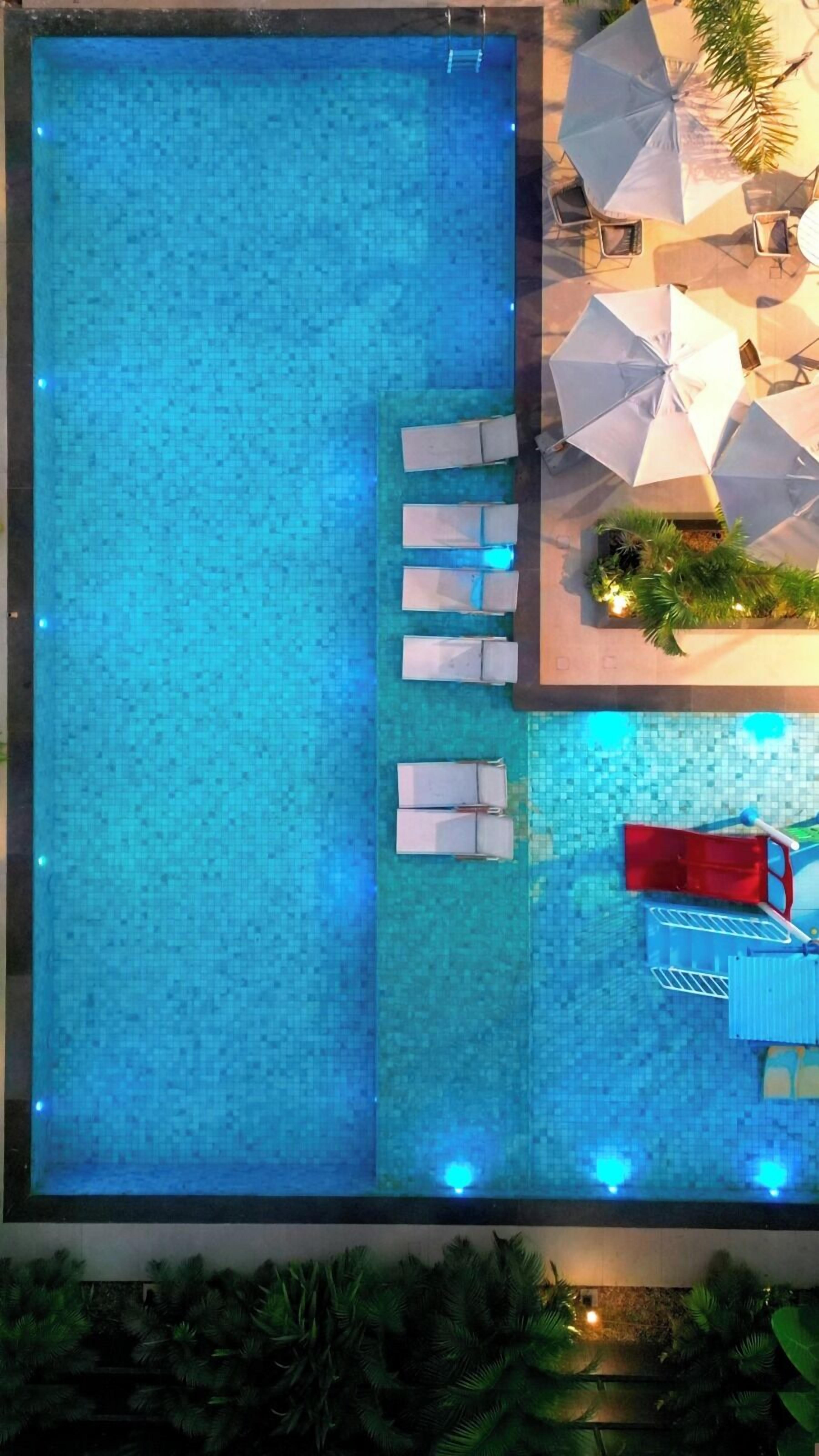 A rooftop pool with clear blue water, surrounded by lounge chairs and umbrellas.