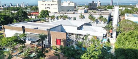 A hotel with a flat roof, surrounded by greenery and palm trees.