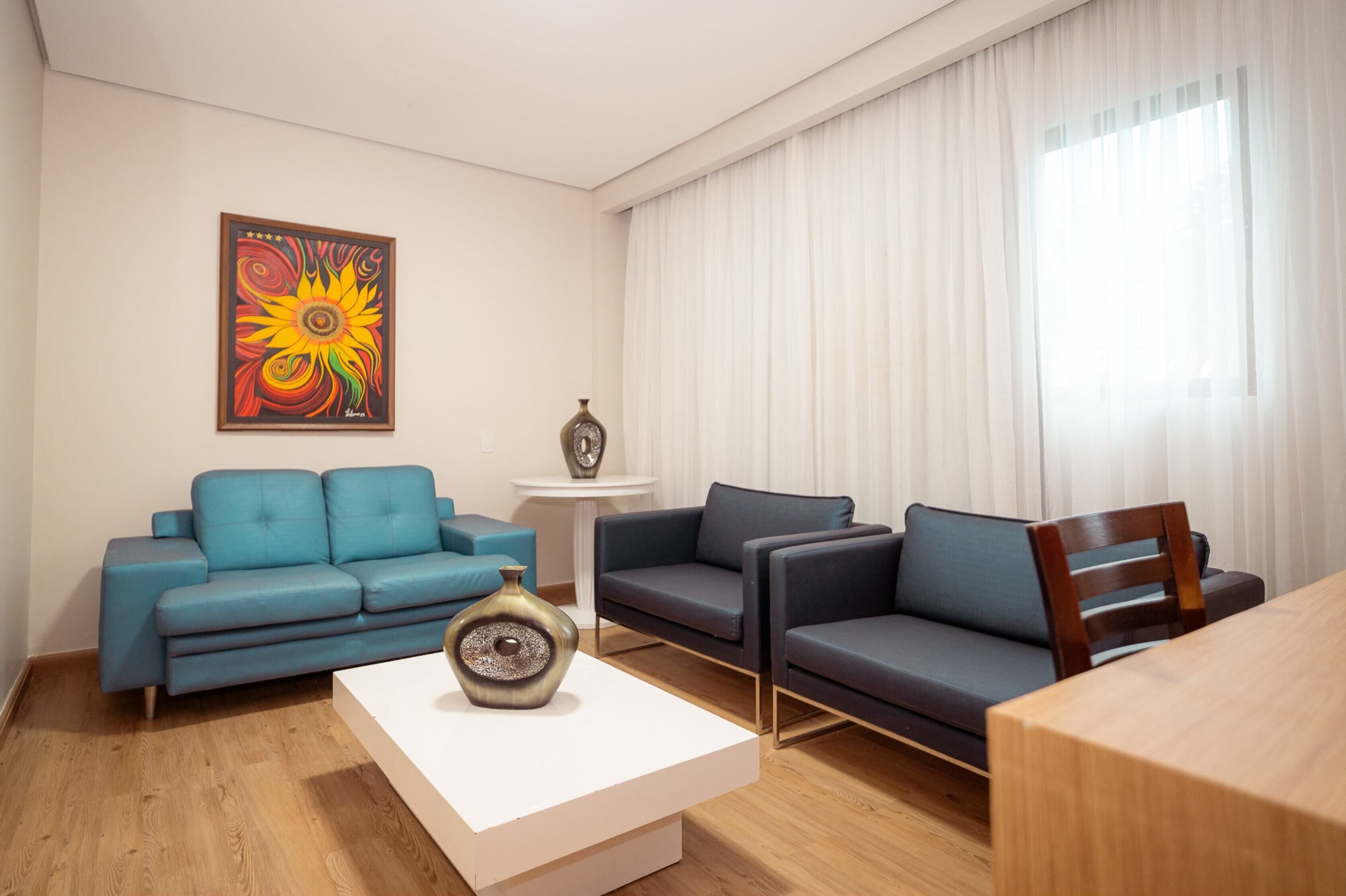 A modern living room with a blue sofa, a dark sofa, a white coffee table, and a vase.