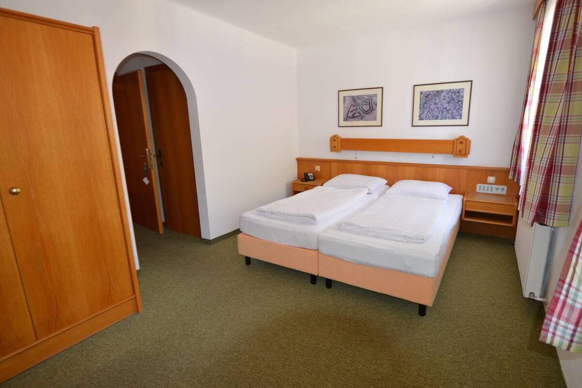 A hotel room with a double bed, a wooden wardrobe, a telephone, and two framed pictures on the wall.