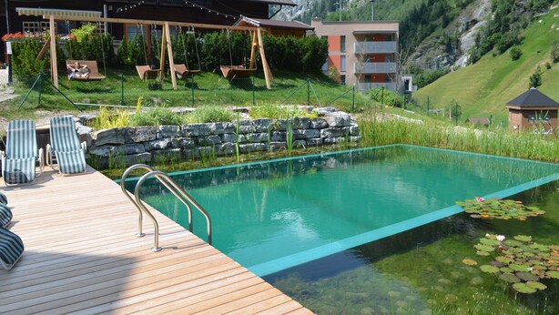 En swimmingpool med træterrasse, liggestole og udsigt til et bjerg.