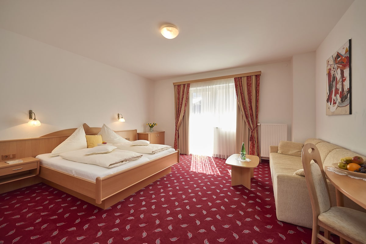 Een hotelkamer met een bed, nachtkastjes, een bureau, een stoel en een raam met gordijnen.