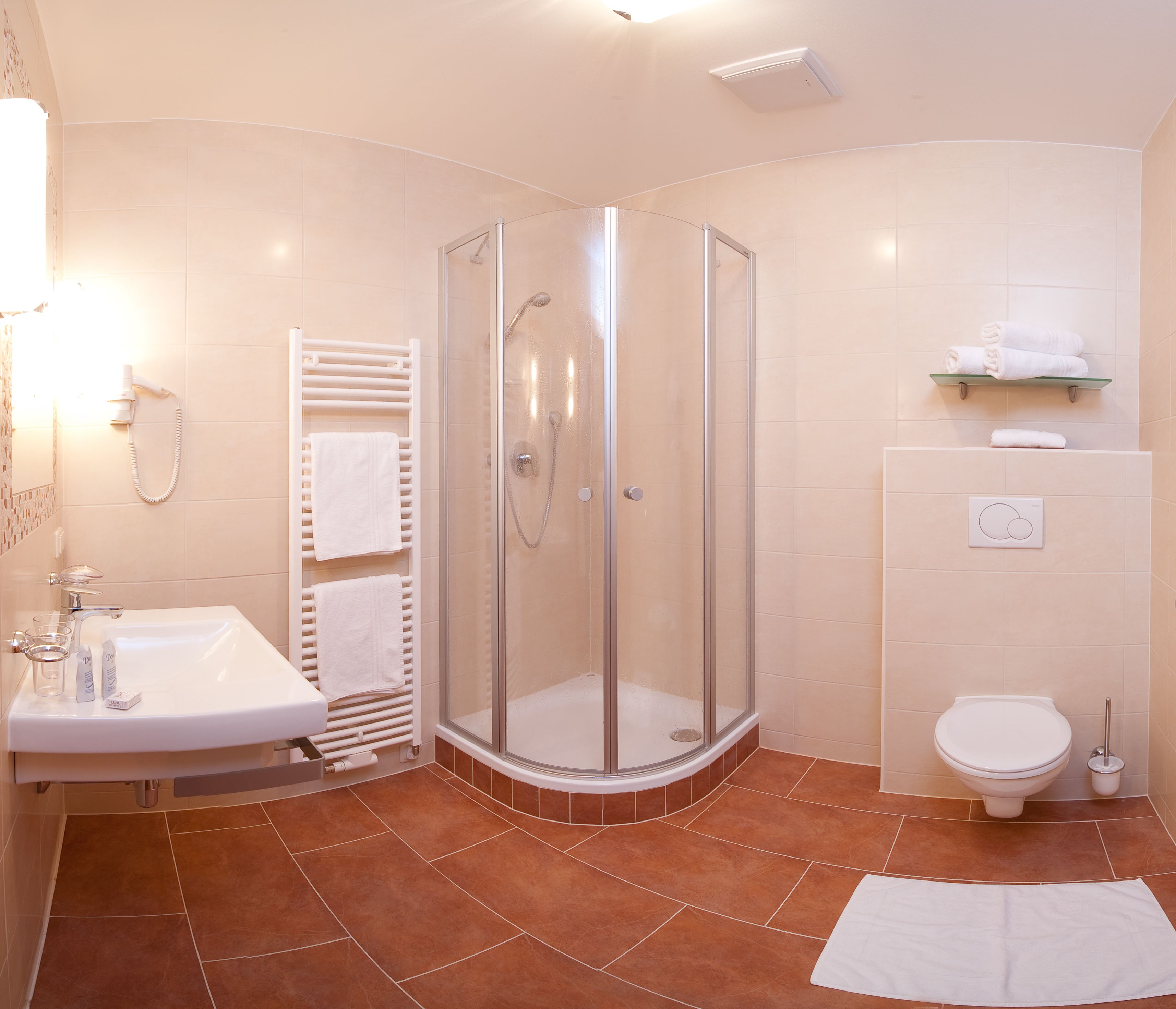 A modern bathroom with a glass-enclosed shower, a white sink with a glass, and a toilet.