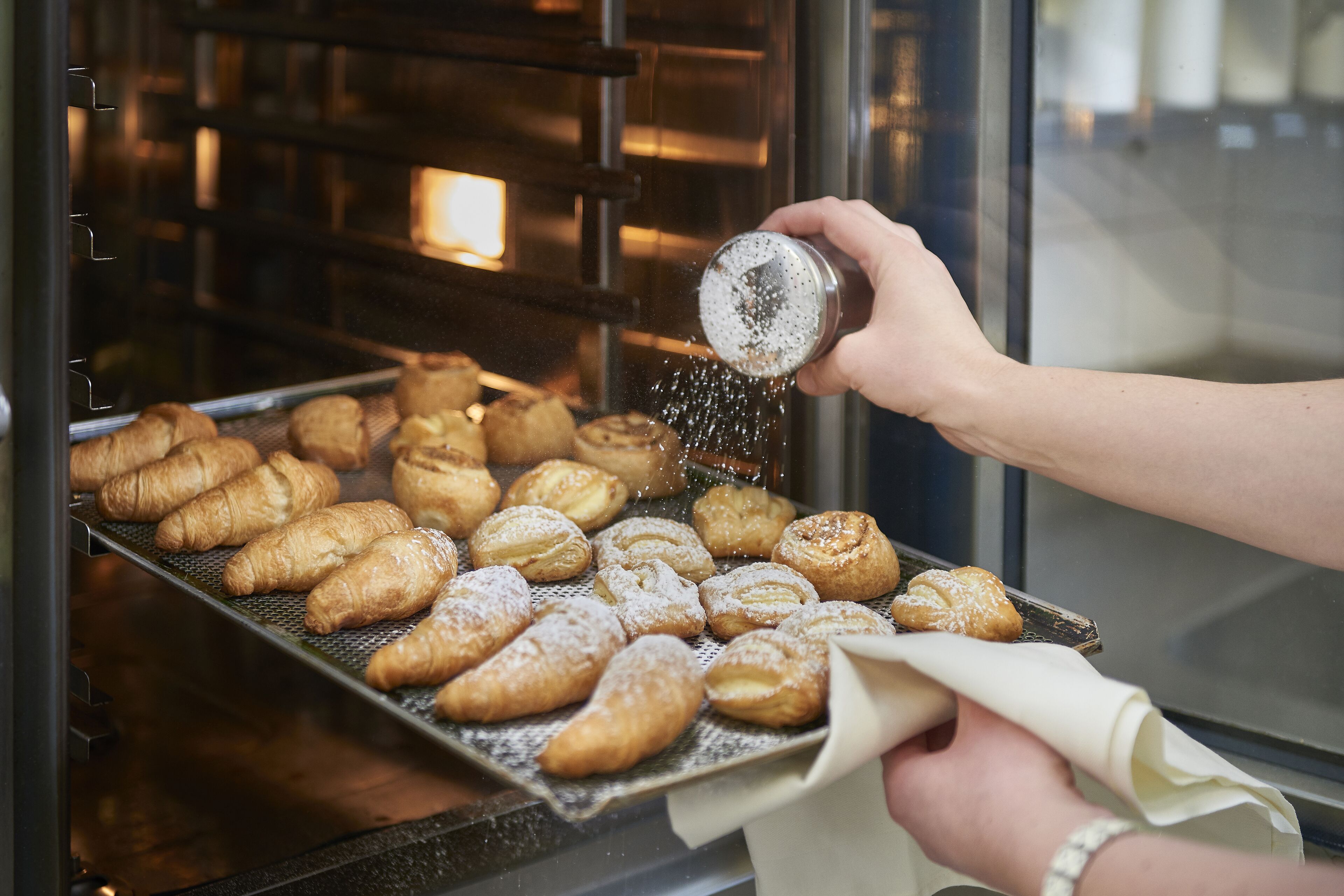 A hand sprinkling powdered sugar on pastries inside an oven.