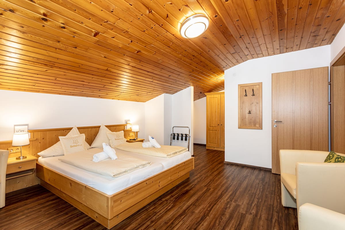 Een hotelkamer met een houten plafond, een groot bed met wit beddengoed, een nachtkastje met een lamp en een houten kledingkast.