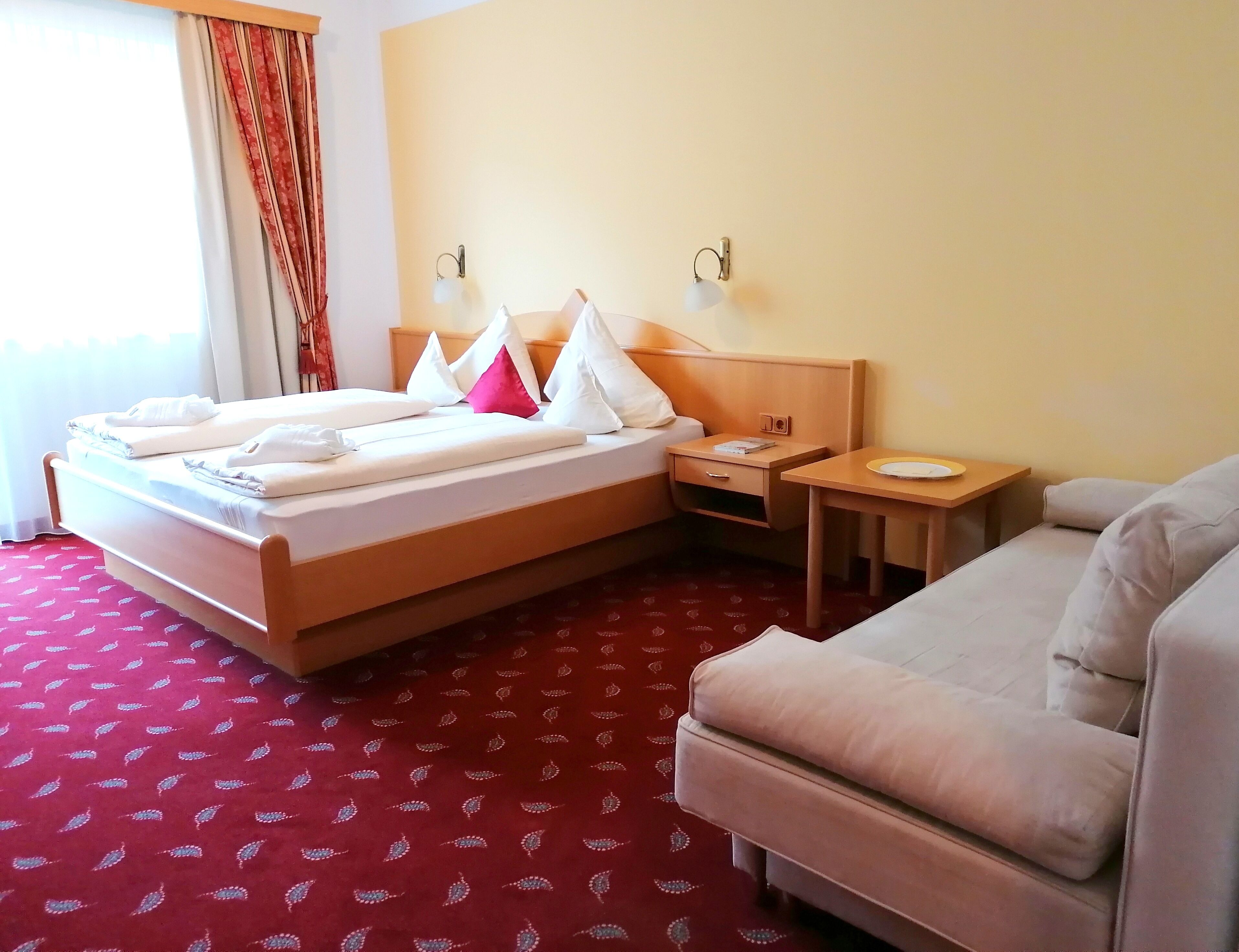 A hotel room with a bed, a bedside table, a small table with a plate, and a sofa.