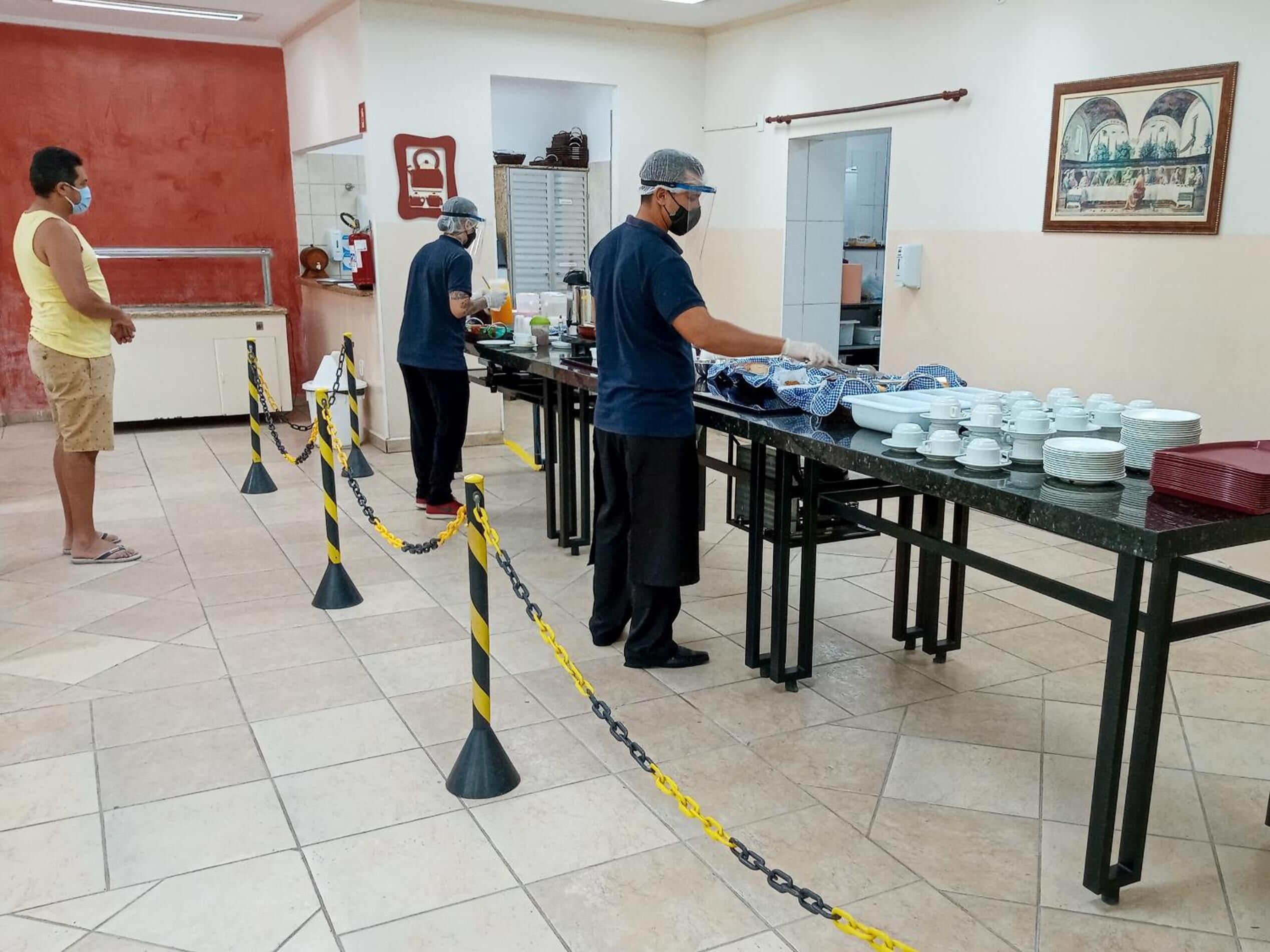 A buffet setup with tables and serving staff, a tiled floor, and a red wall.